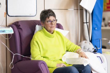 A woman in a green jumper having chemotherapy looking thoughtful
