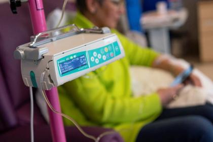 Equipment used in chemotherapy with a woman looking at her phone during her treatment in the background