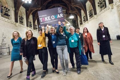 Target Ovarian Cancer campaigners walking through parliament holding a TAKE OVAR placard