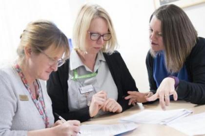 Three female healthcare professionals discuss information at a table