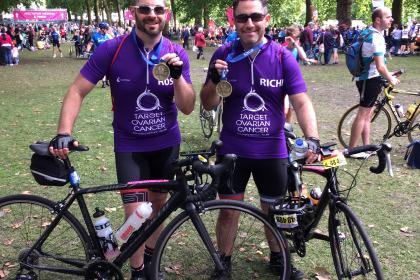 Two Target Ovarian Cancer cyclists at the end of their fundraising event holding their bikes and medals