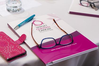 A Target Ovarian Cancer booklet with a pair of glasses on top and a phone next to it in a pink case