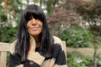 Claudia Winkleman sitting on a park bench looking into the camera