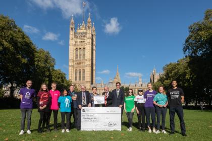 A group of people holding a big cardboard cheque outside of Parliament