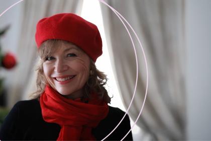 Annie wearing a red beret and red scarf smiling with a Christmas tree in the background
