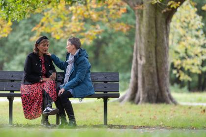 Two people on a park bench with one person putting their hand on the others' shoulder 