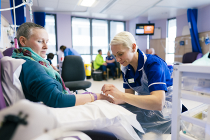 Woman with ovarian cancer in a treatment room looking down as a nurse provides chemotherapy