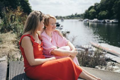 A mother and daughter with arm around shoulder sitting outdoors