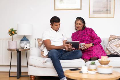 Two people sitting on the sofa looking at an electronic tablet together