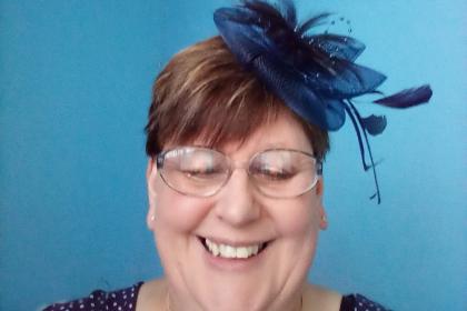 Amanda smiling wearing a blue fascinator in her hair