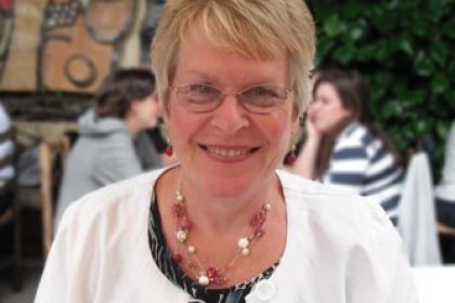 Delia smiling wearing glasses, and printed top and a white cardigan