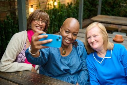 A photo of three women all smiling sitting on a bench taking a selfie together