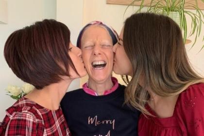Gaby and Chloe standing either side of their mum Amanda kissing her cheeks whilst Amanda has a huge smile