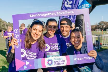Four people smiling inside a Target Ovarian Cancer handheld frame