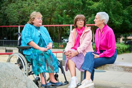 Three women sitting together outside, one in a wheelchair