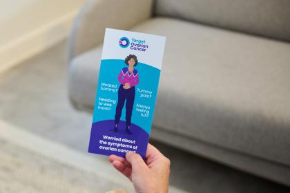 Someone holding out a symptoms awareness information leaflet from Target Ovarian Cancer