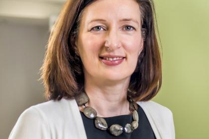A headshot image of Professor Fiona Thistlethwaite wearing a dark top, white cardigan and necklace