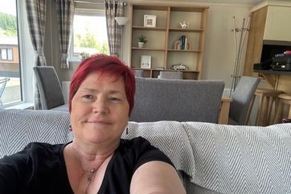 Lorraine, a lady with red hair sitting on her sofa taking a selfie and smiling