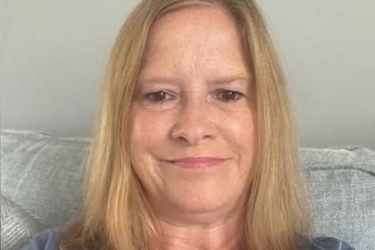 A selfie that Judy is taking sitting on her sofa wearing a blue patterned top with her blonde hair worn down and she's smiling