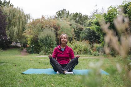 A woman in the park practicing yoga on a teal coloured yoga mat