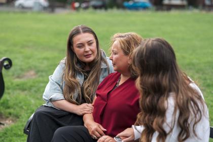 Woman and her daughters sitting on bench arm in arm