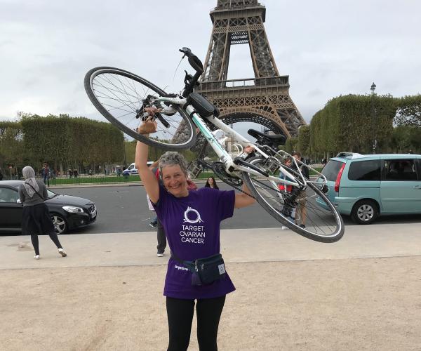 Sara, a Target Ovarian Cancer fundraiser, holding her bike up in the air in front of the Eiffel Tower