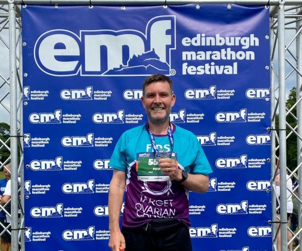 A Target Ovarian Cancer fundraiser smiling and holding a medal after taking part in the Edinburgh Marathon Festival