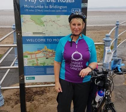A target ovarian cancer fundraiser smiling next to her bike at the seafront