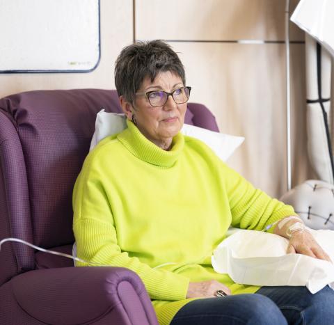 A woman in a green jumper having chemotherapy looking thoughtful
