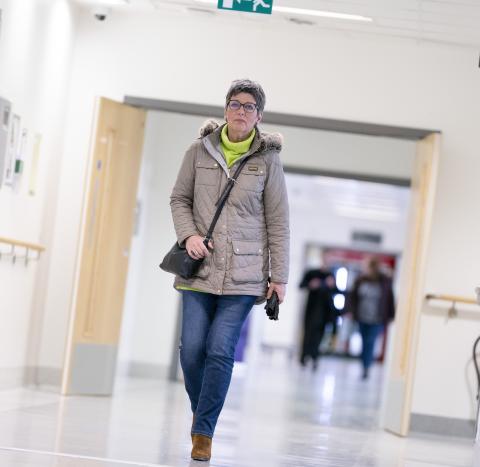 A woman with ovarian cancer wearing a coat and green jumper walking down a hospital corridor