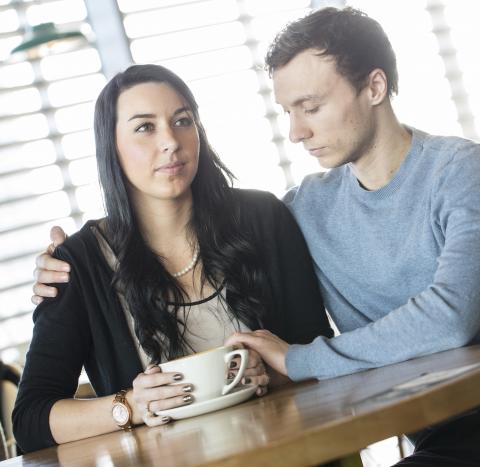 A man comforting a woman while having a cup of coffee