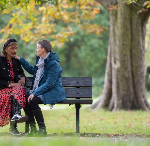 Two people on a park bench with one person putting their hand on the others' shoulder 