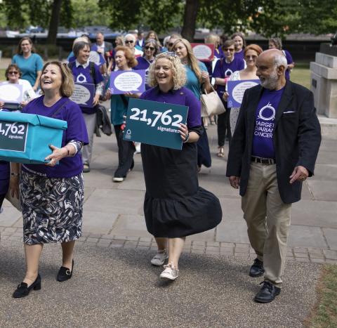 A group of people walking outside parliament building holding poster supporting Target Ovarian Cancer
