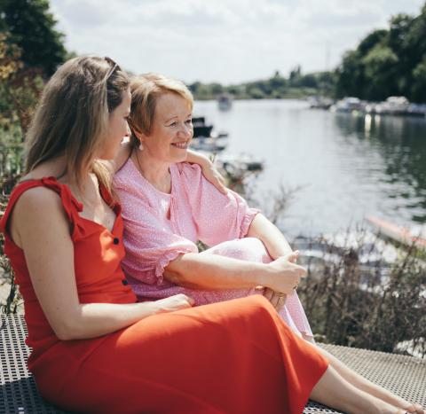 A mother and daughter with arm around shoulder sitting outdoors