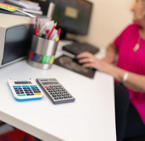 Woman at a computer with calculator in the foreground