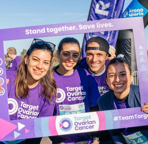 Four people smiling inside a Target Ovarian Cancer handheld frame