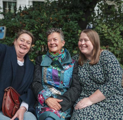 A photo of three women sitting on a bench taking a selfie, all smiling