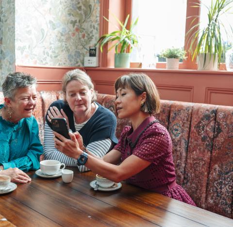 Three women sitting at a table looking at a phone together