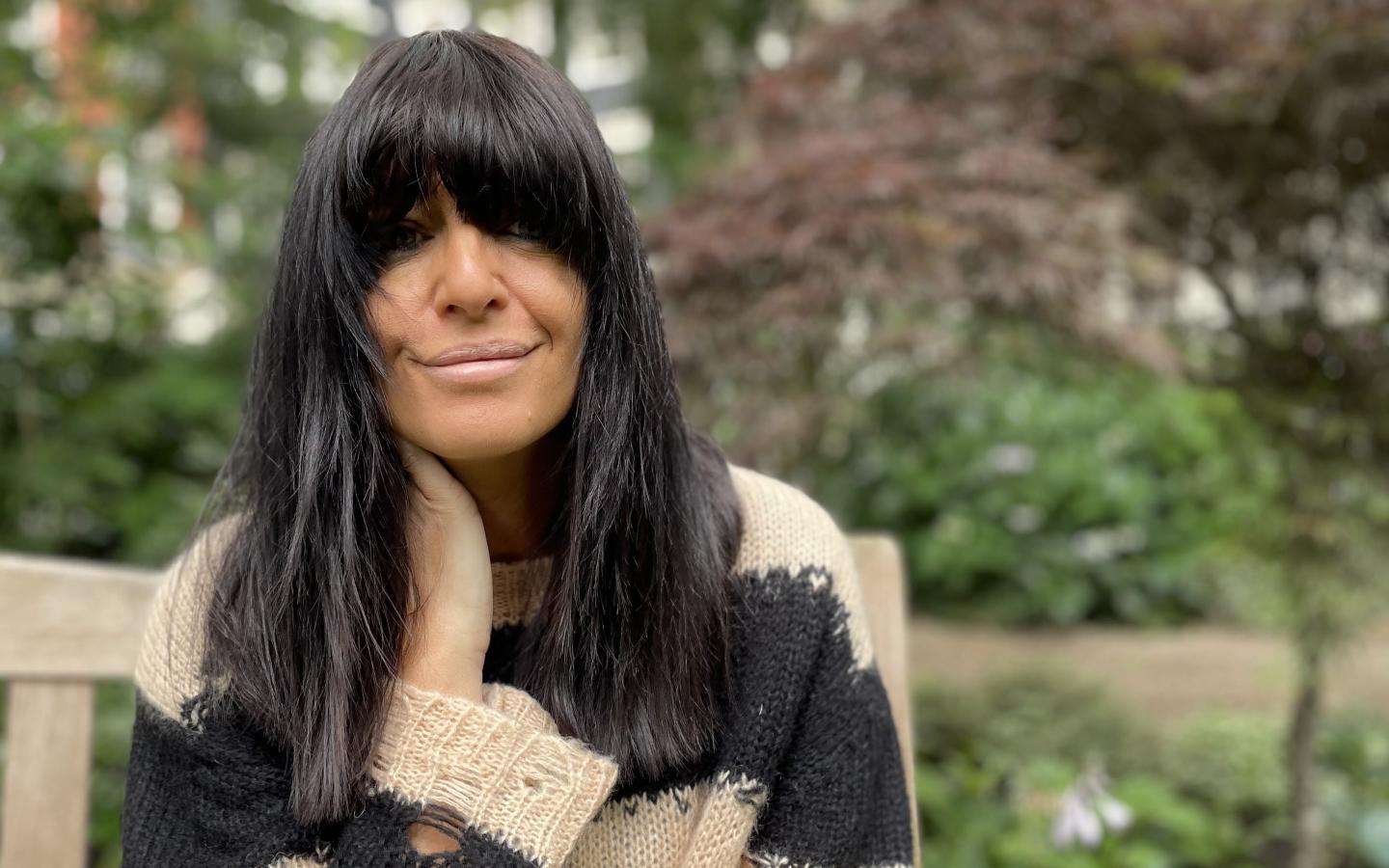 Claudia Winkleman sitting on a park bench looking into the camera