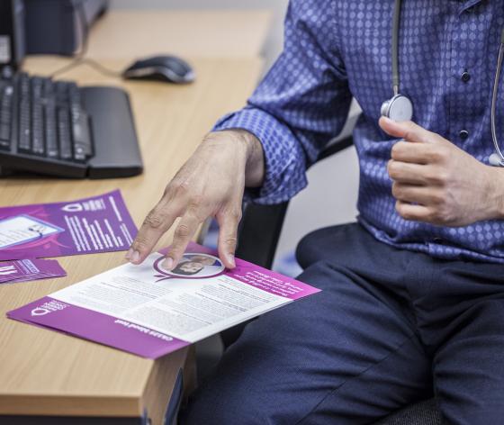 A GP using his hands to talk through a Target Ovarian Cancer leaflet on his desk