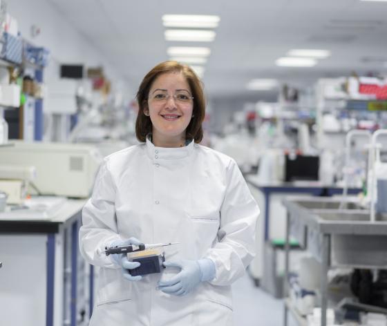 An ovarian cancer researcher smiling and holding lab equipment