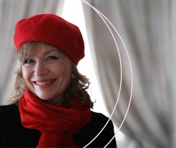 Annie wearing a red beret and red scarf smiling with a Christmas tree in the background