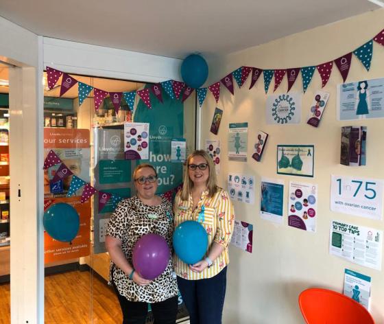 Two colleagues doing workplace fundraising with Target Ovarian Cancer bunting, banner and balloons in their workplace