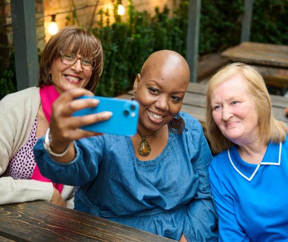 A photo of three women all smiling sitting on a bench taking a selfie together