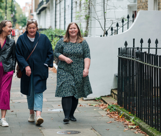 Three women walking down the street together all chatting a smiling