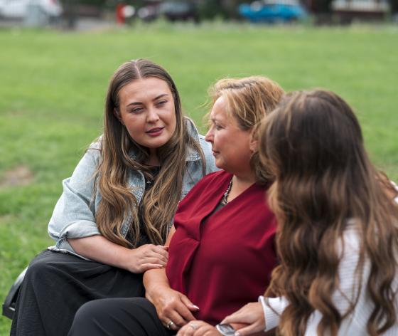 Woman and her daughters sitting on bench arm in arm