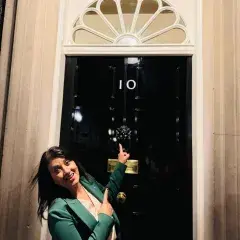 Reeta standing outside 10 Downing Street - smiling and pointing at the door.