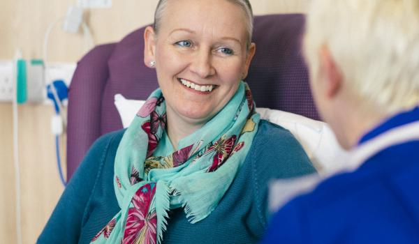 A woman smiles at a nurse while having chemotherapy
