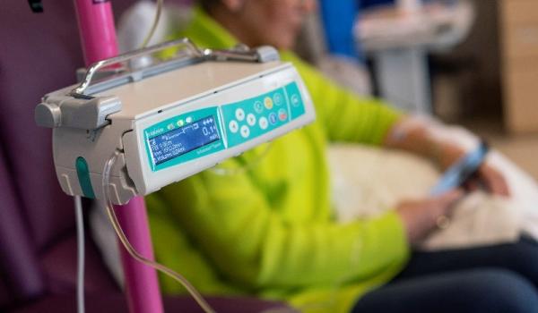 Equipment used in chemotherapy with a woman looking at her phone during her treatment in the background