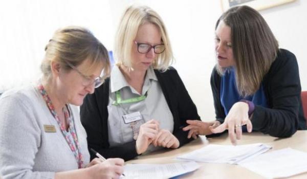 Three female healthcare professionals discuss information at a table